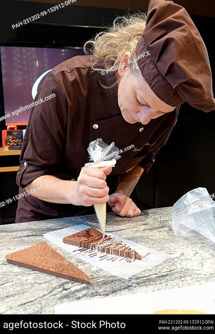 PRODUCTION - 13 November 2023, Switzerland, Broc: Chocolatière Géraldine Müller Maras decorates a homemade triangular chocolate bar with liquid chocolate in the...