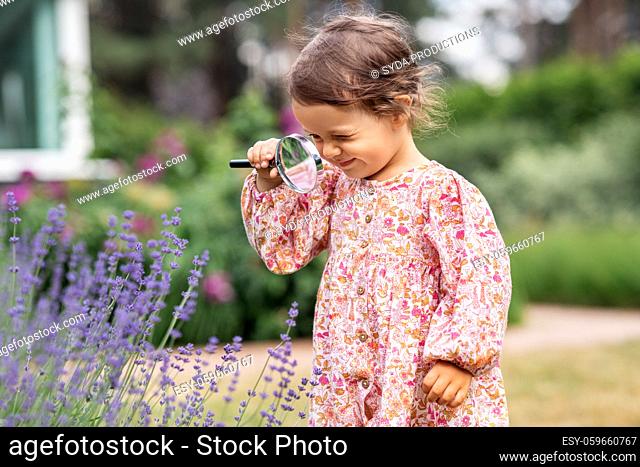 baby girl with magnifier looking at garden flowers