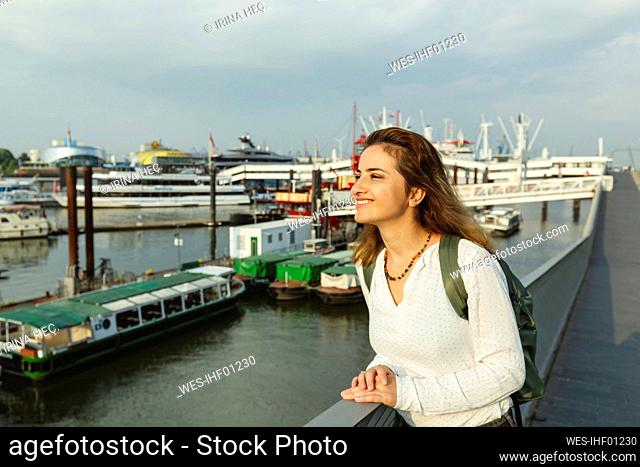Happy woman standing by railing on sunny day at Port of Hamburg, Germany