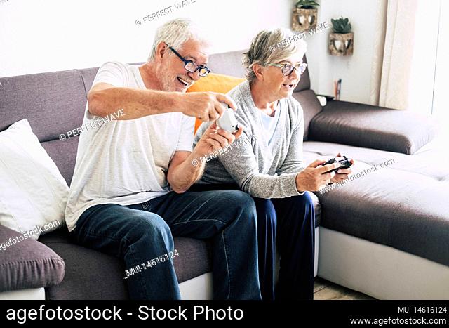 couple of seniors and mature people looking and the tv and using controllers playing video games at home together on the sofa - lockdown lifestyle indoors