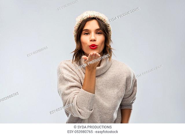 young woman in knitted winter hat sending air kiss