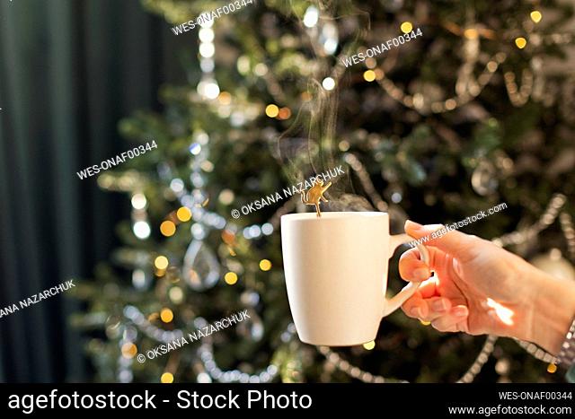 Woman's hand with cup of tea by decorated Christmas tree