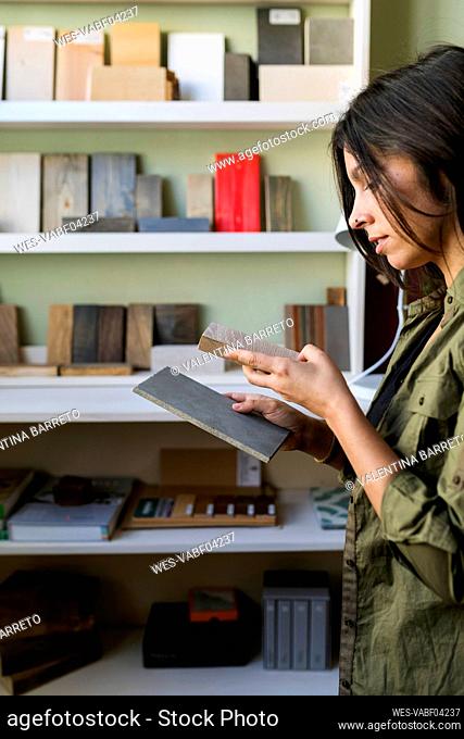 Craftswoman examining wooden samples while standing by shelf in industry