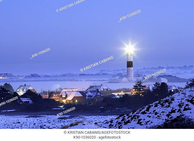 Lighthouse Kampen on snow covered fields in operation with the light beam visible, seen from abvoe with the traditional houses of the village of Kampen and a...