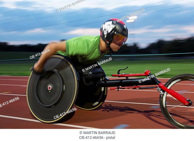 Determined young male paraplegic athlete speeding along sports track in wheelchair race