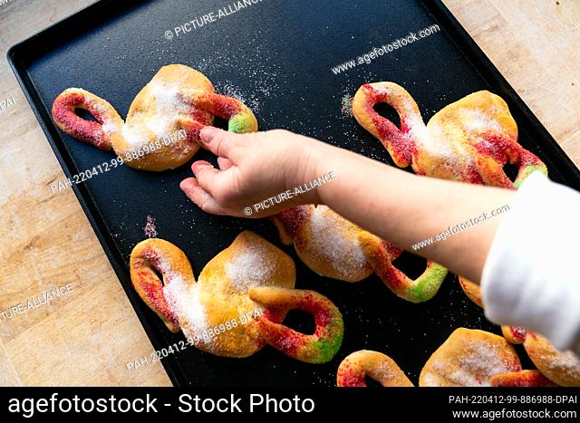 PRODUCTION - 11 April 2022, Bavaria, Ostheim Vor Der Rhön: A woman places an ""Easter stork"" made of yeast dough and colored sugar on a baking tray