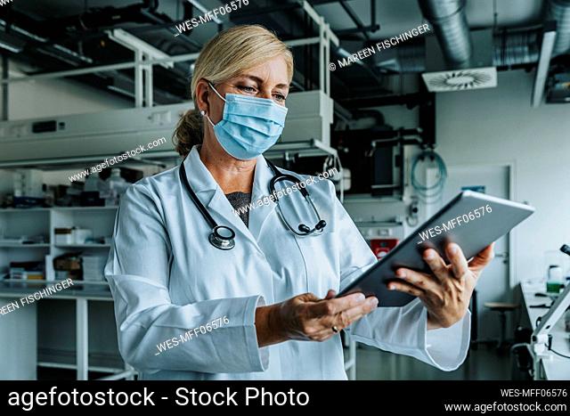 Scientist wearing face mask using digital tablet while standing at laboratory