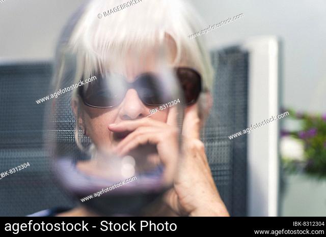 Concept alcoholism, portrait of a senior citizen behind a wine glass, sunglasses, balcony, Grevenbroich, North Rhine-Westphalia, Germany, Europe