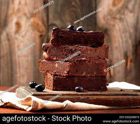 stack of square baked slices of brownie chocolate cake with walnuts on a wooden surface. Cooked homemade food. Chocolate pastry