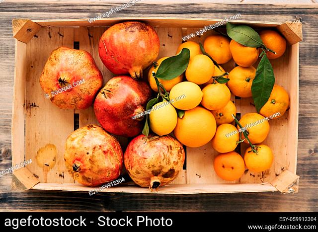 A wooden box with tangerines, lemons and pomegranates. Fruits collected in the autumn garden. High quality photo