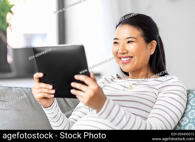 happy pregnant asian woman with tablet pc at home