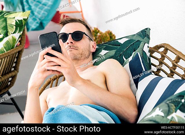 Man wearing towel using mobile phone while relaxing on sofa at patio