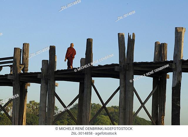 Monk walking at Sunrise over the lake near wooden foot bridge U Bein Bridge crossing the Taungthaman Lake near Amarapura in Mandalay Myanmar