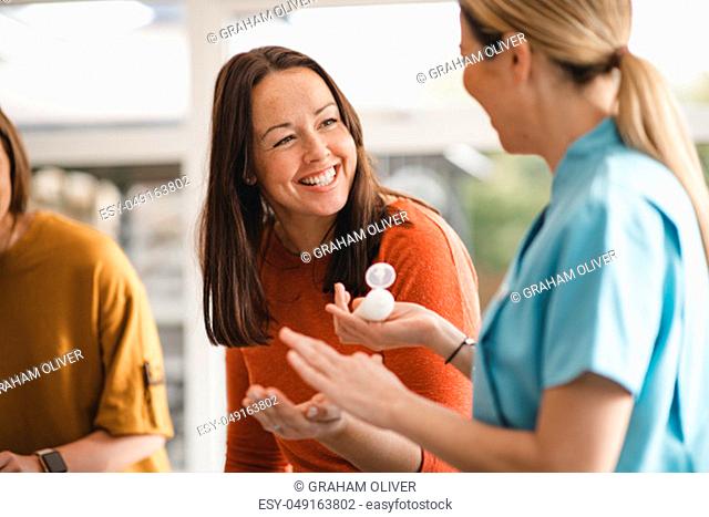 Mid adult woman speaking to a beauty product sales representative at a product party. She is sampling a beauty product