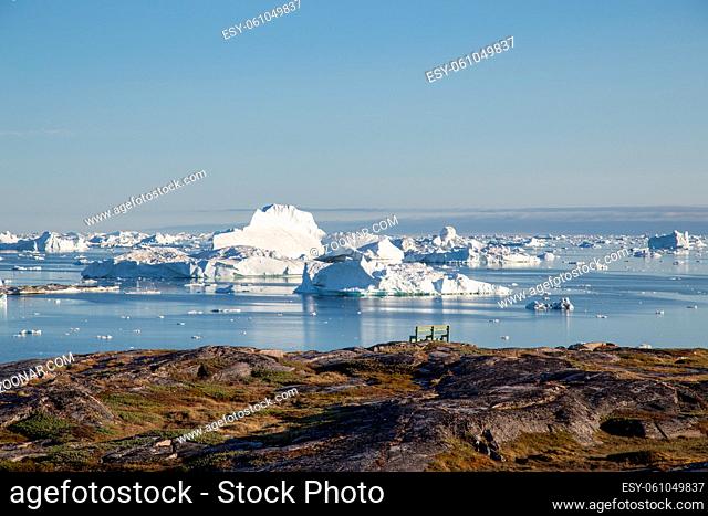 Ilulissat, Greenland - July 9, 2018: A bench at the coastline with iceberg view. Rodebay, also known as Oqaatsut is a fishing settlement north of Ilulissat