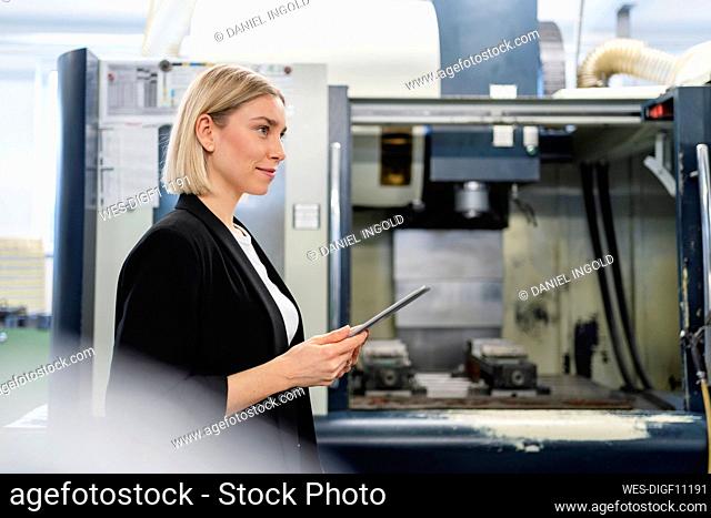 Smiling woman holding tablet in factory hall