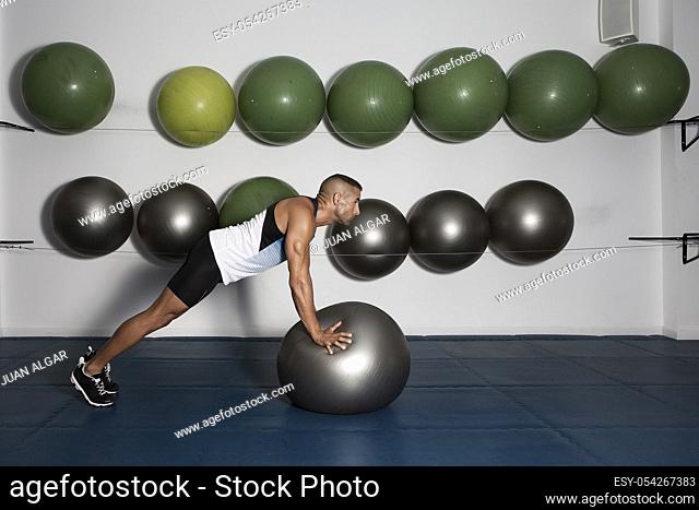 Side view of focused strong man in sportswear training with medicine ball in modern gym