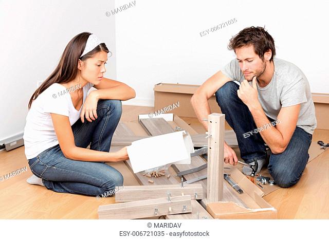 Couple moving in assembling bed furniture with problems and difficulties. Young interracial couple in new home. Asian woman, Caucasian man
