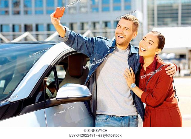 Happy moments. Cheerful happy couple taking selfies while standing near their car
