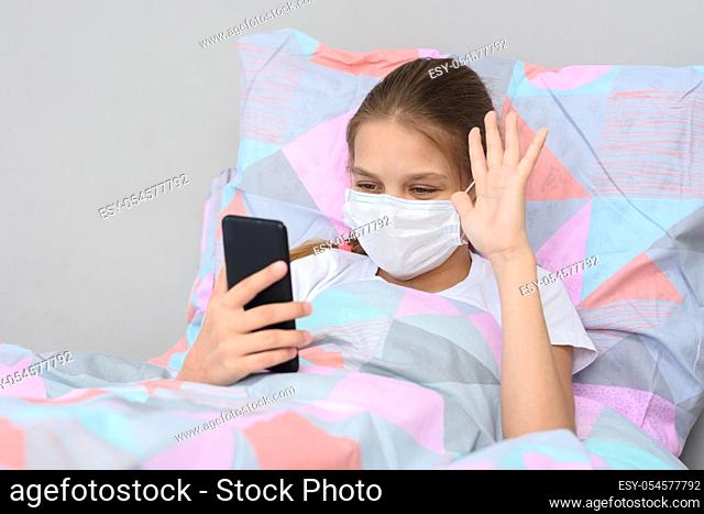 A sick girl lies in bed and communicates with friends online via video-telephone