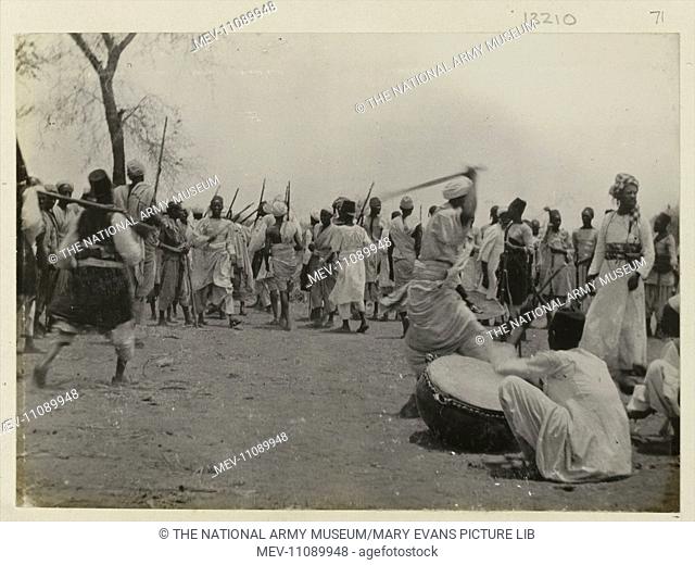 Photograph of Sudanese preparing for battle. Photograph from an album associated with the 2nd Sudan War (1896-1899). Men with swords and shields gather around...