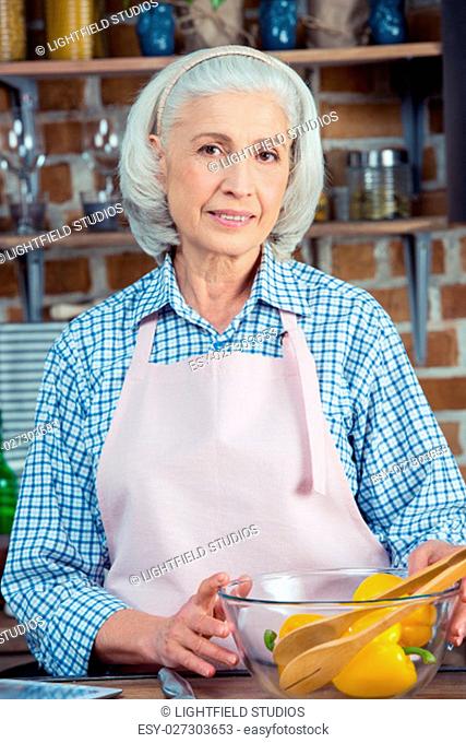 Attractive senior woman in apron smiling at camera in kitchen