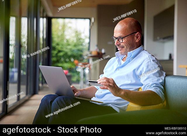 Smiling senior man paying through credit card on laptop at home
