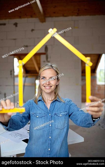 Smiling female architect making house shape with folding ruler at construction site