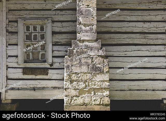 An abandoned log cabin with a stone chimney flue, cracked and dried out wood cladding and broken window