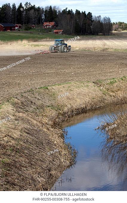 New Holland 8770 tractor with harrows, harrowing field seedbed beside small river, Sweden, may