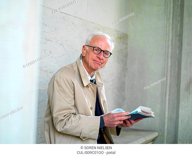 Senior man in raincoat reading newspaper, portrait, Copenhagen, Hovedstaden, Denmark