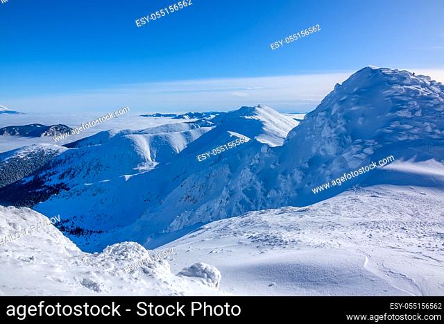A lot of snow on the peaks and slopes of the winter mountains. Sunny weather and cloudless blue sky