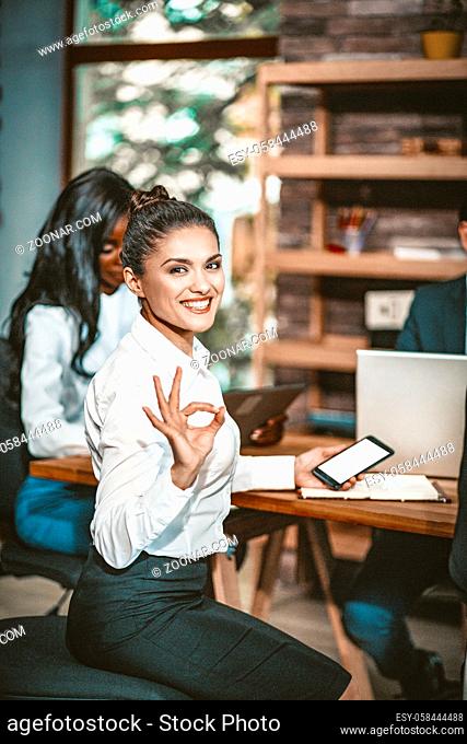 Smiling Businesswoman Showing Ok Sign, Intelligent Woman Shows Okey Gesture Meaning That Everything Will Be Good With One Hand And Holding Phone In Other Hand