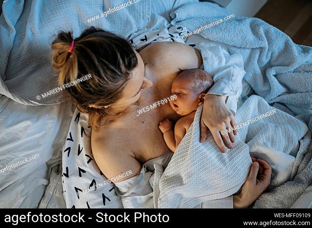 Baby sleeping on mother's chest in bed at home