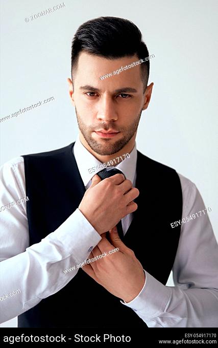 Young handsome man in elegant suit adjust his necktie on white background