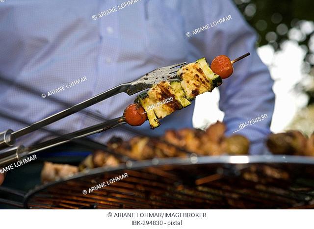 A vegetable spit on a grill, getting turned-over by the cook