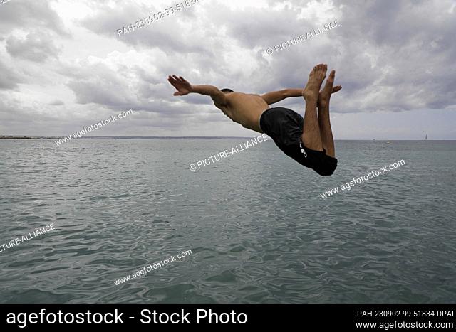 02 September 2023, Spain, Palma: Osman jumps into the sea on a cloudy day at Can Pere Antoni beach, where a yellow alert has been issued for possible severe...