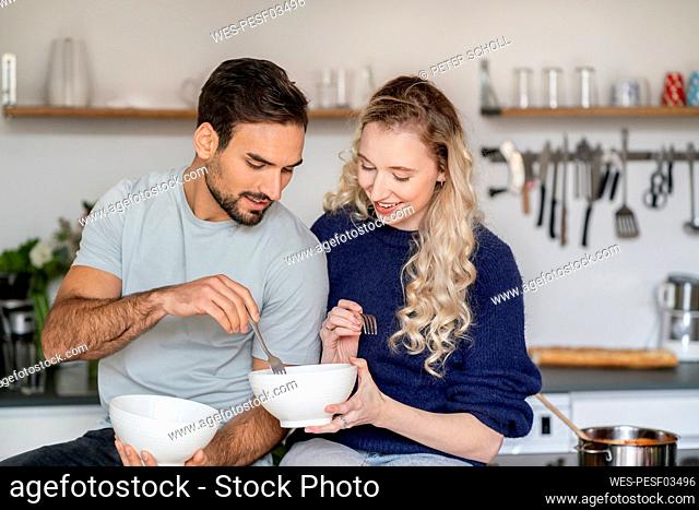 Smiling young woman sharing food with boyfriend in kitchen at home