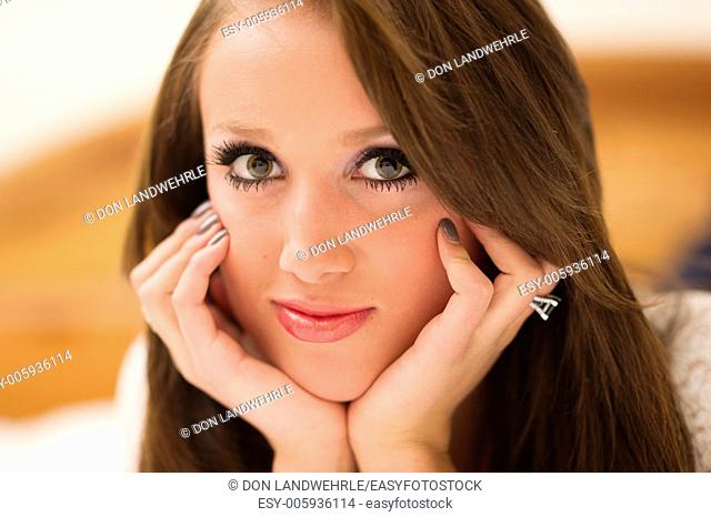 Attractive teenage girl resting her head in her hands lying on a bed