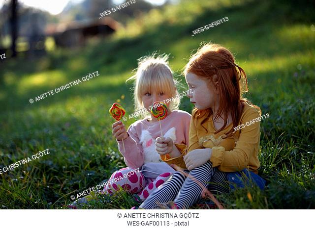Two sisters sitting in a field holding lollipops