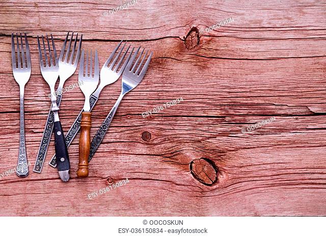 Random pile of assorted rustic forks arranged on the side of a rustic wooden table with copyspace in a concept of country cuisine, overhead view