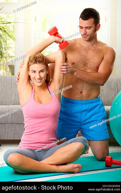 Couple doing dumbbell exercise sitting on fittness mat at home, smiling