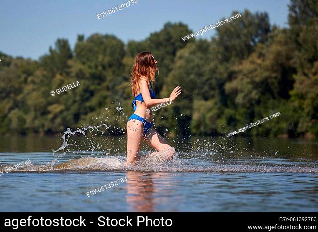 Young woman running into splashing water at the beach