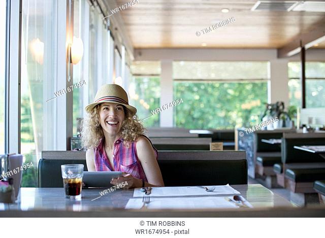 A woman in a hat sitting in a diner, holding a digital tablet