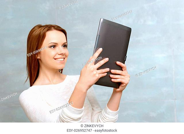 Using technologies. Young smiling woman looking at her tablet on isolated background
