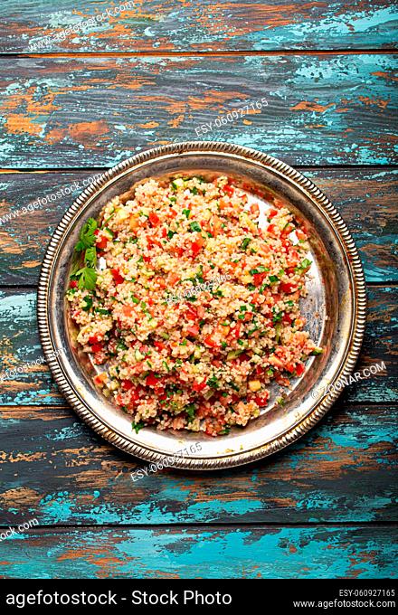 Middle eastern and Mediterranean traditional vegetable salad tabbouleh with couscous on rustic metal plate and wooden background from above