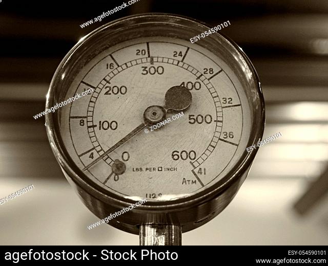 sepia monochrome image of an old shiny brass round pressure gauge with a round dial marked in numbers
