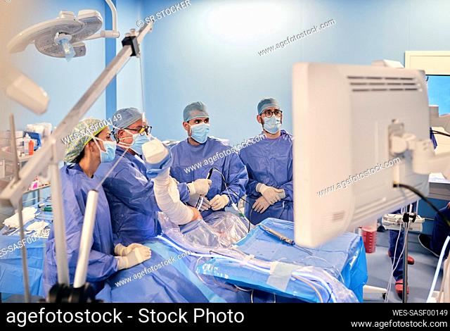 Surgeons in face mask and medical scrubs operating arthroscopic surgery while standing at operation room during COVID-19