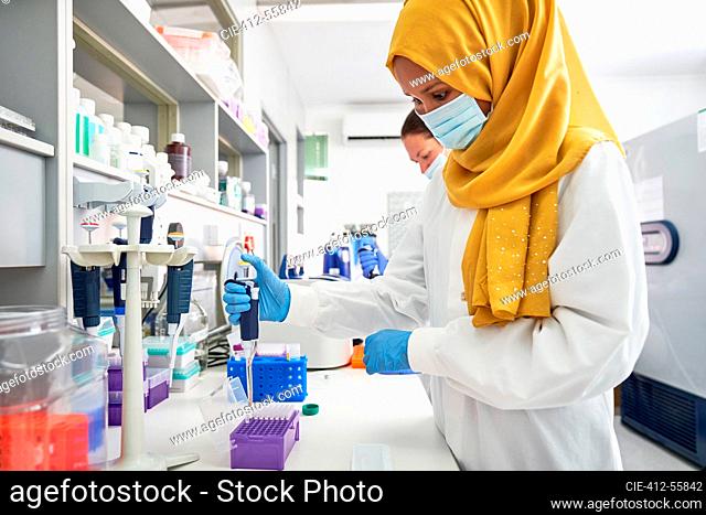 Female scientist in hijab and face mask using pipette in laboratory