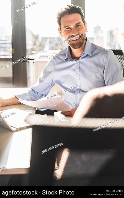 Smiling businessman using laptop while having discussion with colleague at office